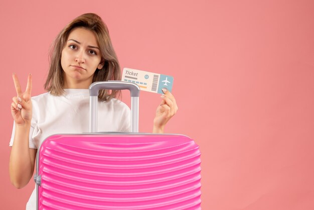 upset young girl with pink suitcase holding ticket making victory sign