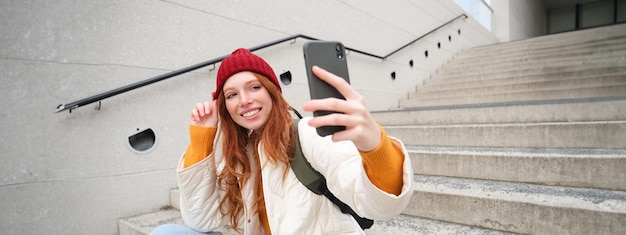 Free Photo urban girl takes selfie on street stairs uses smartphone app to take photo of herself poses for