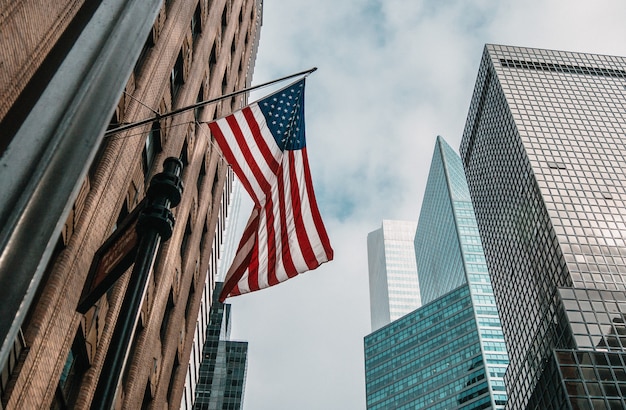 The USA or United States of America flag on a flagpole near skyscrapers under a cloudy sky