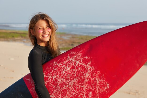 Vacation, lifestyle, tourism concept. Satisfied boardsurfer in wetsuit, carries waxed board