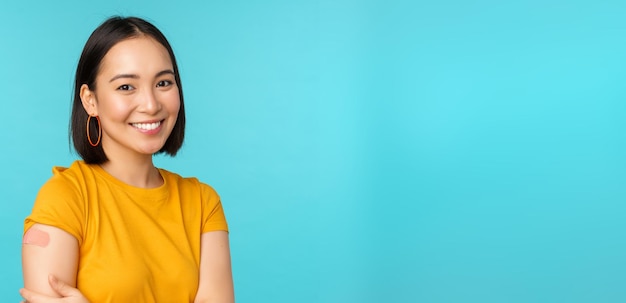 Vaccine campaign from covid19 Young beautiful healthy asian woman showing shoulder with bandaid concept of vaccination standing over blue background