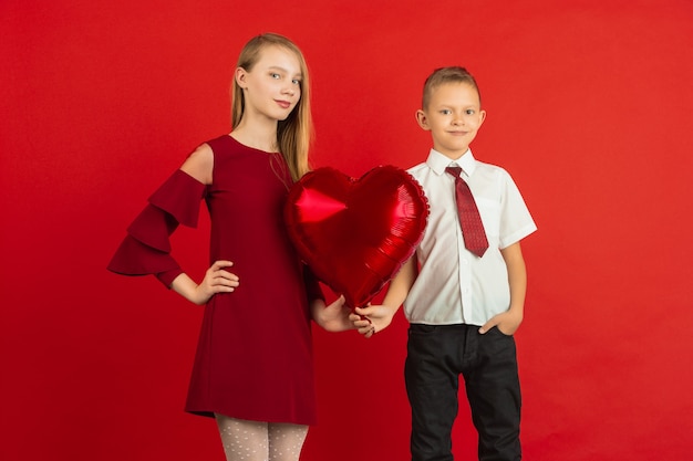 Valentine's day celebration, happy, cute caucasian kids isolated on red studio