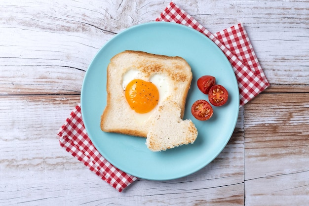 Free photo valentines day breakfast with egg with tomatoes heart shaped and toast bread on wooden tablexa