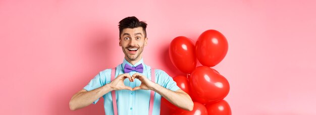 Free Photo valentines day concept romantic guy looking happy and smiling showing heart gesture to lover on spec