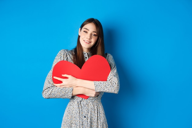 Valentines day dreamy romantic woman hugging big red heart cutout looking sensual at camera standing...