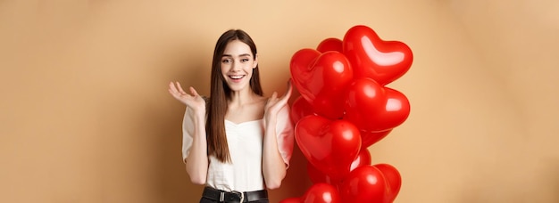 Free photo valentines day and love concept happy smiling woman raising hands up surprised standing near romanti