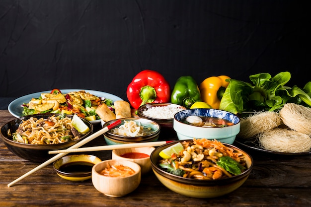 Variation of thai cuisine with bell peppers and bokchoy on wooden desk against black background