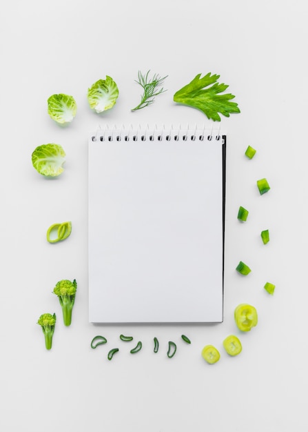 Free photo varieties of chopped vegetables surrounding spiral notepad on white backdrop