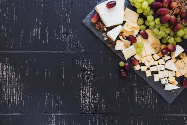 Variety of cheese blocks with grapes on black textured backdrop