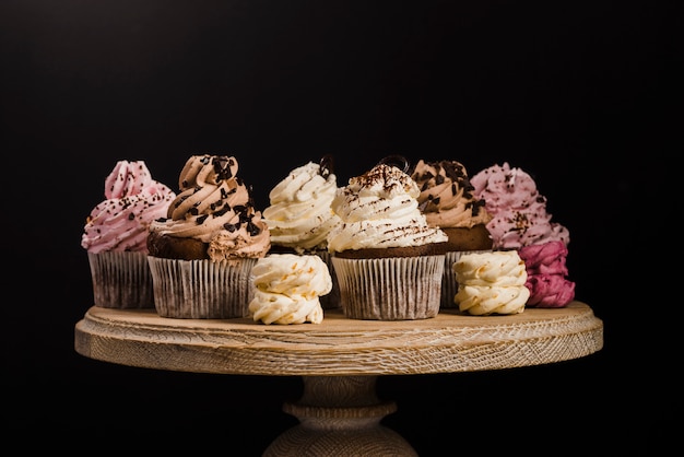 Free photo variety of cupcakes on wooden cakestand against black background