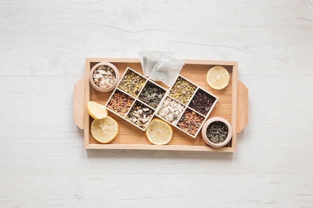 Variety of herbs and dried chinese chrysanthemum flowers arranged in small container on wooden tray