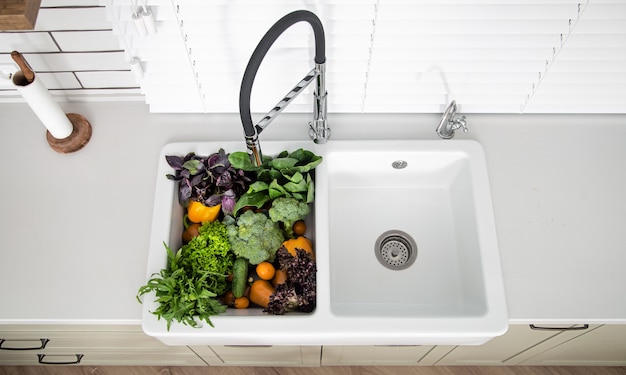 Variety of vegetables in the kitchen sink of modern kitchen close up.