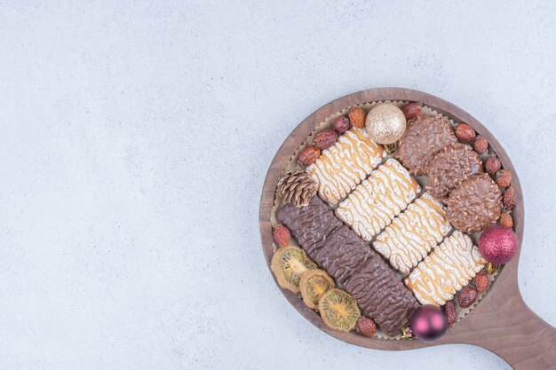 Various biscuits, dried fruits and Christmas baubles on wooden board. 