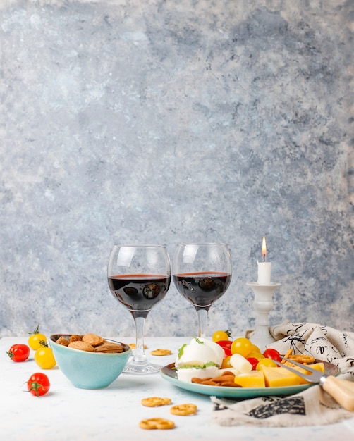 Free Photo various cheese and cheese plate on light table with different nuts and fruits and glass of wine