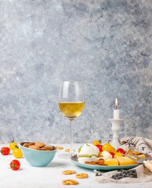 Various cheese and cheese plate on light table with different nuts and fruits and glass of wine