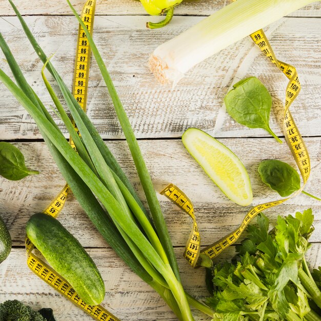 Various green healthy food with measuring tape on wooden plank