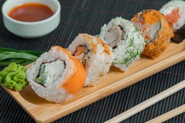 Various kind of sushi on wooden board with sauce.