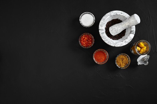 Various oriental spices and white marble mortar on black background with copy space. Still life. Flat lay. Top view.