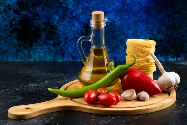 Free photo various pasta, oil and vegetables on wooden board.