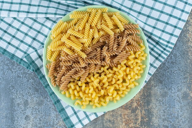 Various pastas in bowl on the towel, on the marble surface. 