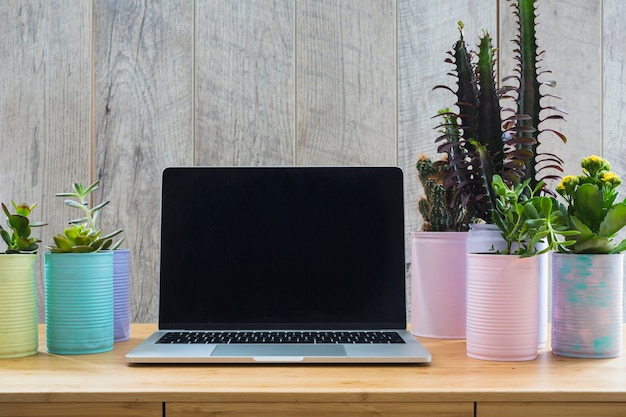 Free Photo various plant in the painted recycle cans with an open laptop on wooden table