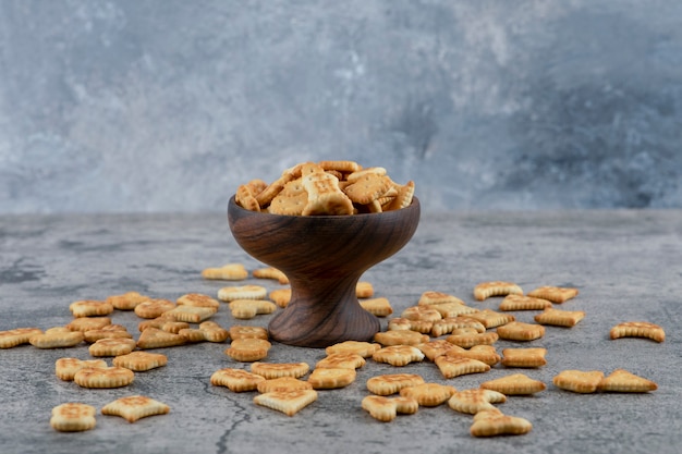 Various small crackers in wooden bowl and scattered on marble background.