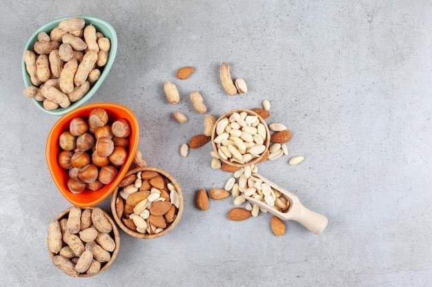 Various types of nuts in bowls and scattered next to scoop on marble background. High quality photo