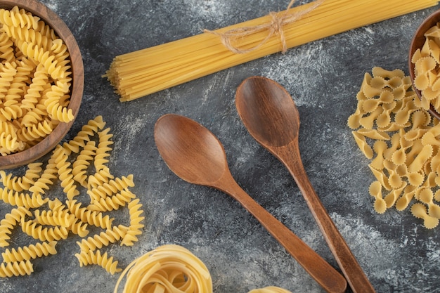 Various types of uncooked pasta with wooden spoons. 