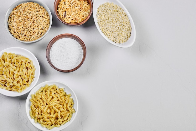 Various uncooked pasta bowls on white with flour.