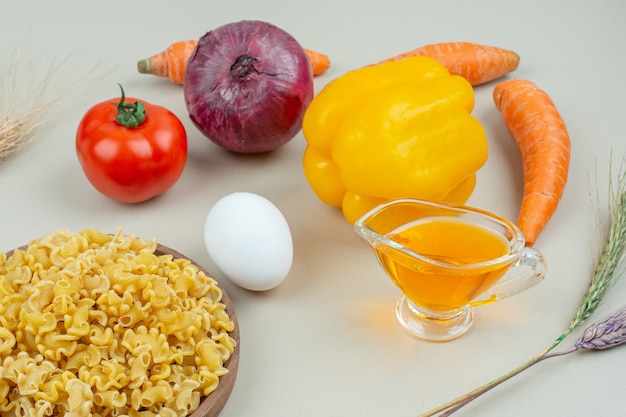 Various vegetables next to pasta in a bowl, on the marble.