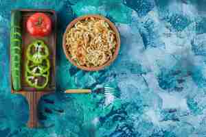 Free photo variously vegetables on a board next to fork an a bowl of noodle on the blue table.