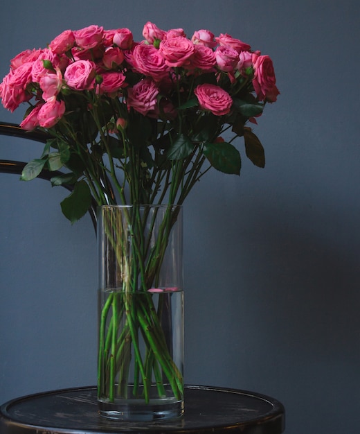 Free photo a vase of pink roses standing on an old rustic round ottoman chair