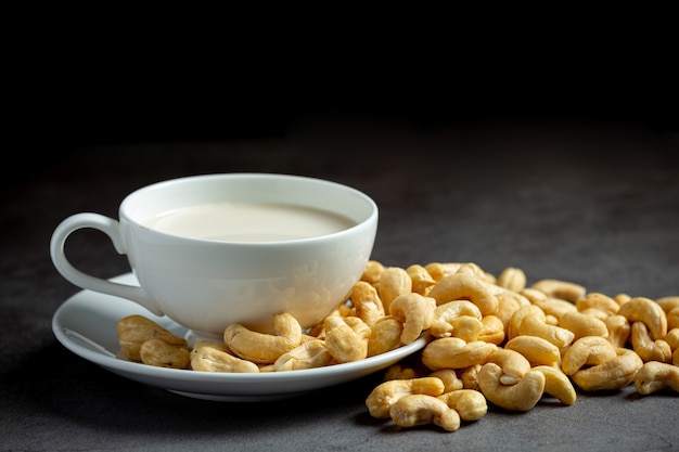 Vegan cashew milk in glass with cashews nuts on dark background