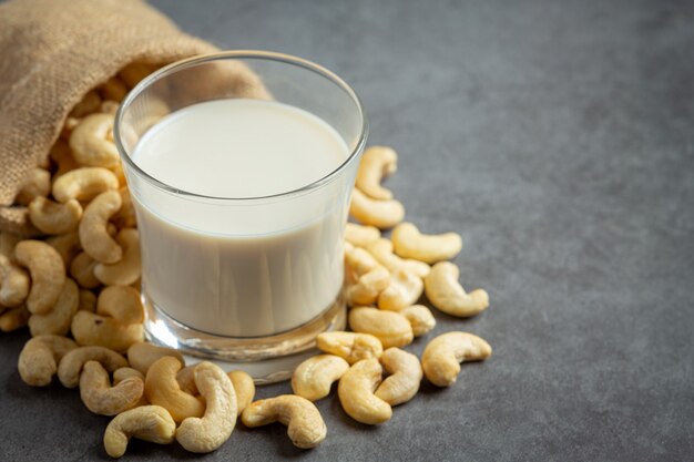 Vegan cashew milk in glass with cashews nuts on dark background