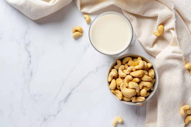 Vegan cashew milk in glass with cashews nuts on marble background