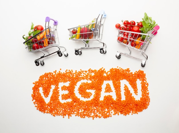 Free photo vegan lettering with delicious vegetables in small shopping carts