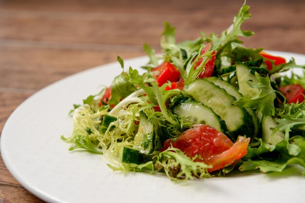 Vegetable salad in white round plate on wooden table.