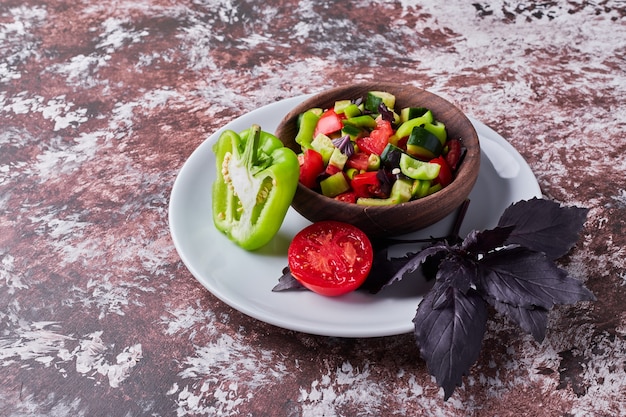 Vegetable salad in a wooden cup on the marble in the middle, angle view.