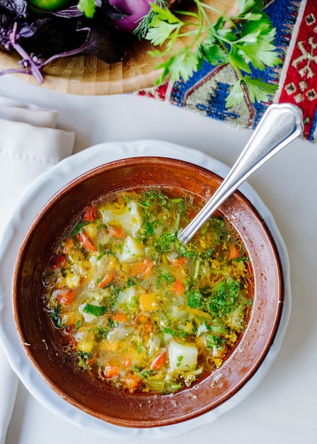 Free photo vegetable soup with herbs inside brown bowl.