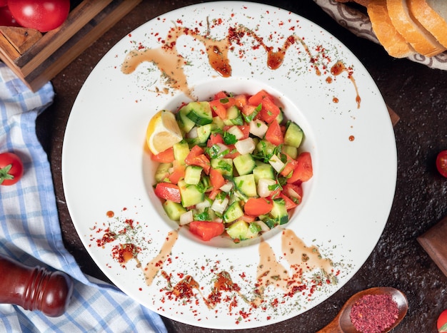 Vegetable, tomatoes, cucumber, roka salad. salad with sumakh and lemon on the kitchen table inside white plate