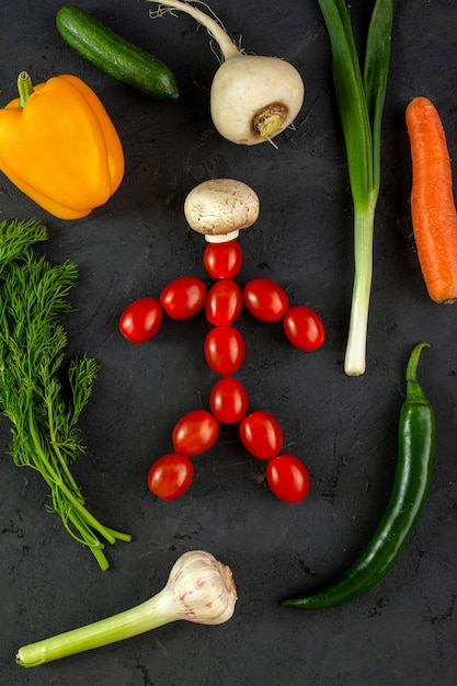 Vegetables fresh ripe mellow colorful vegetables along with human shaped red cherry tomatoes with white champignon on grey floor