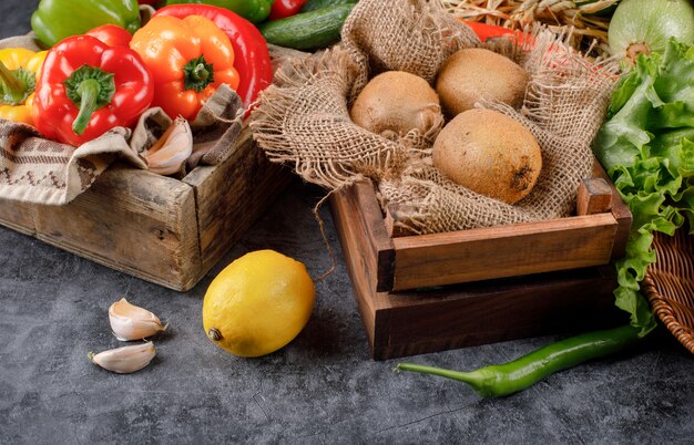 Vegetables and kiwies in a wooden tray with lemon and garlics around.