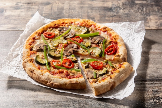 Vegetarian pizza with zucchini tomato peppers and mushrooms on wooden table