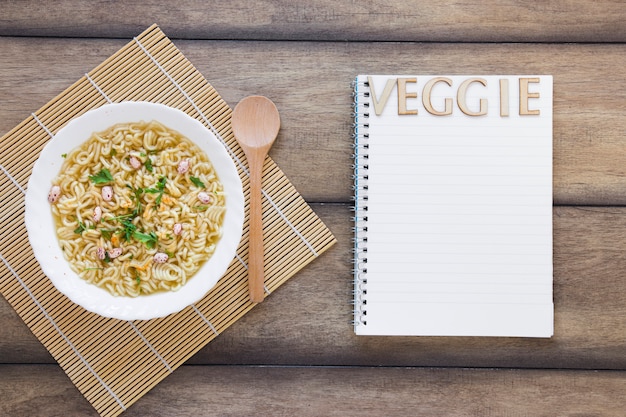 Free photo veggie soup next to veggie lettering on notebook