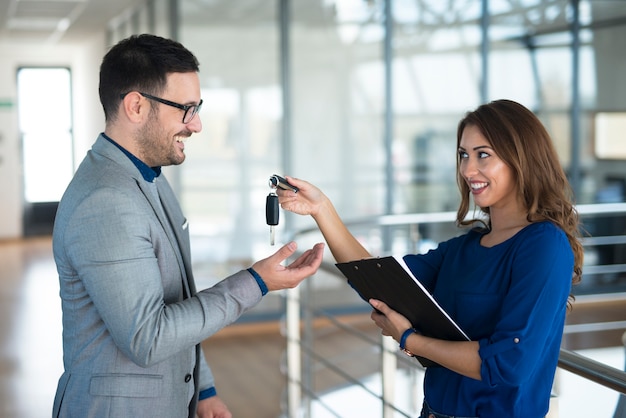 Vehicle dealer giving keys to the car buyer in showroom