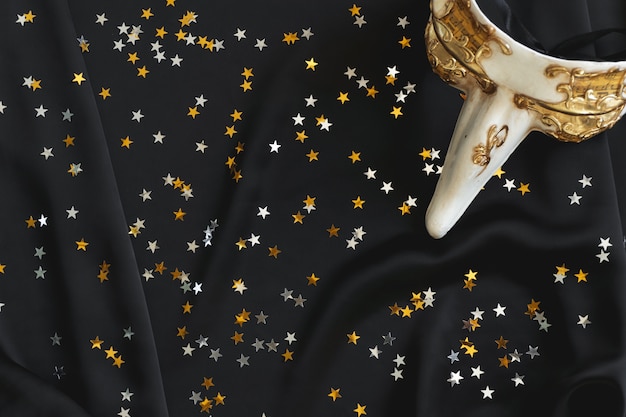 Venetian mask with a long nose on a black fabric with star confetti