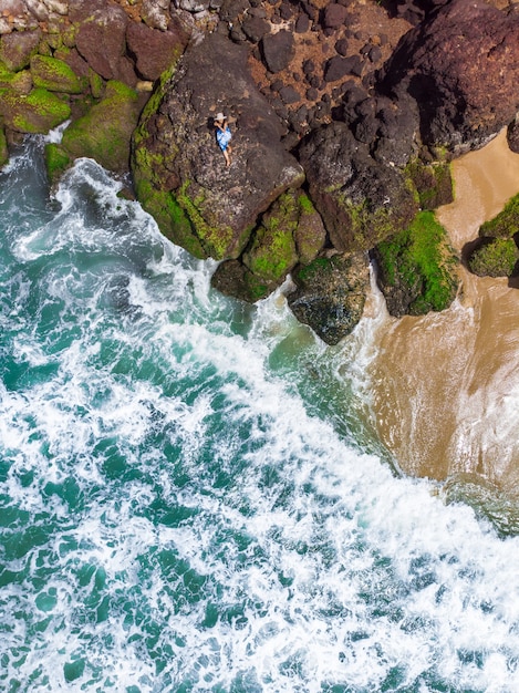 Free photo vertical aerial shot of a female with blue dress lying on the rocky beach