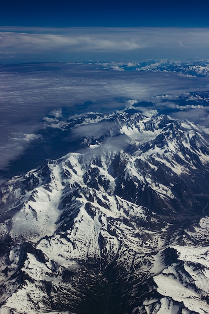 Vertical aerial shot of snowy mountainous scenery under the breathtaking blue sky