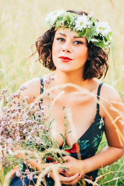 Vertical  of the Caucasian woman with a wreath with flowers collecting flowers in the field