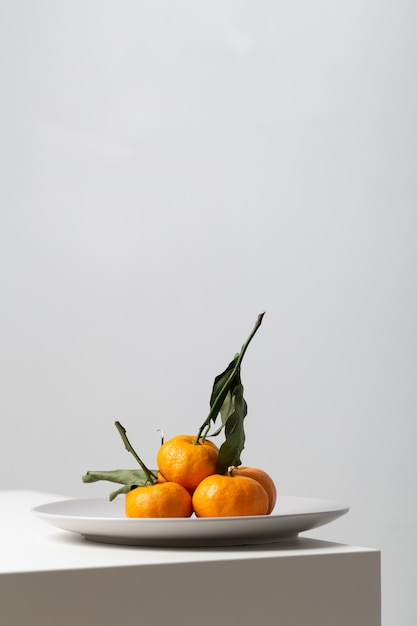 Free Photo vertical closeup of mandarines on a plate on the table under the lights on white